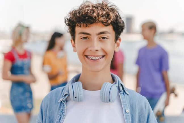 Teen with braces and headphones smiling outdoors, representing the ideal timing for wisdom teeth removal during summer break